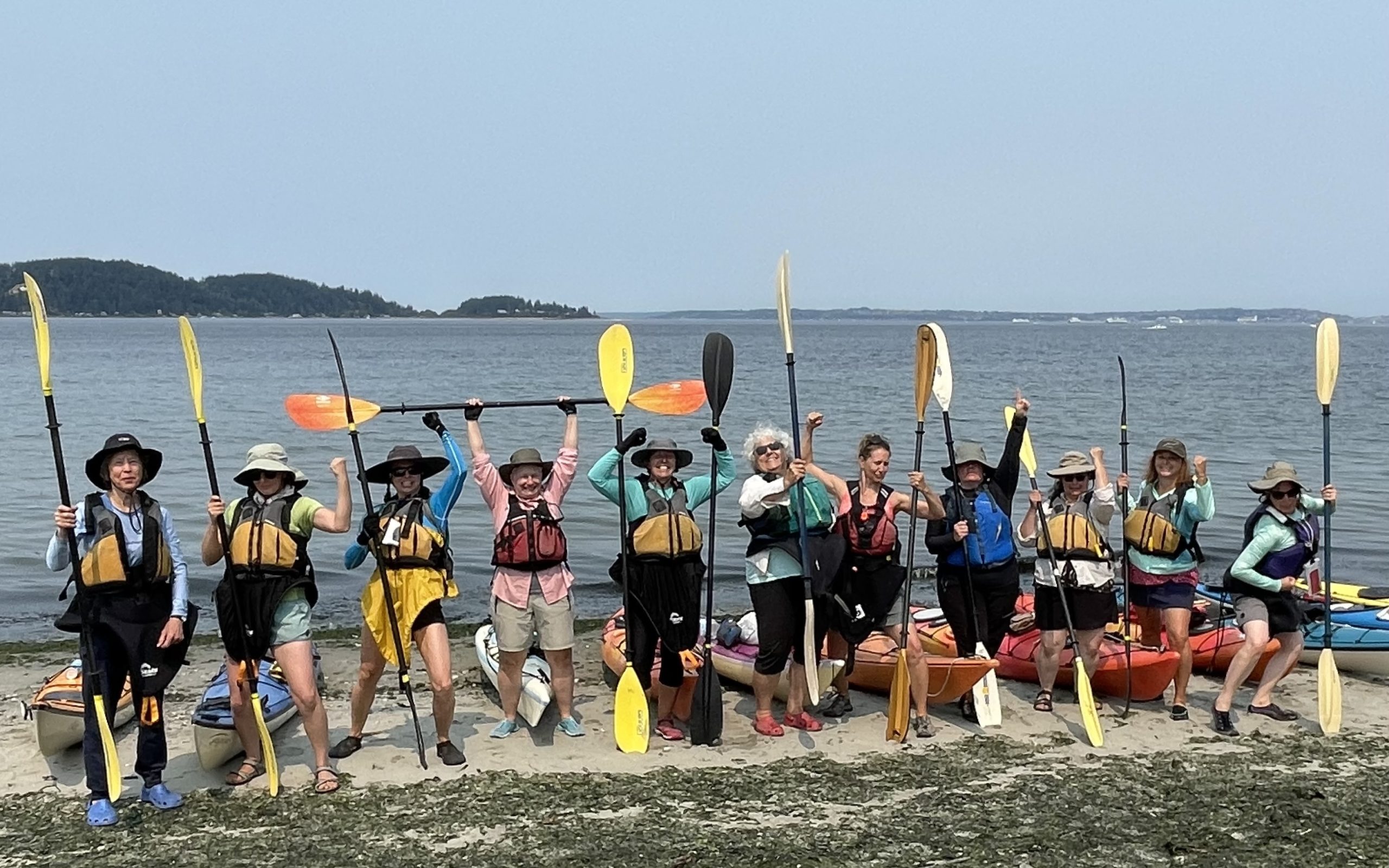 Powerful women kayaking with paddles raised on shore